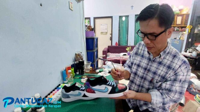 
					KREATIF: Rinto Oluan Kusuma Situmorang (44) saat memperagakan sepatu lukisannya (Foto: Ainul Jannah).