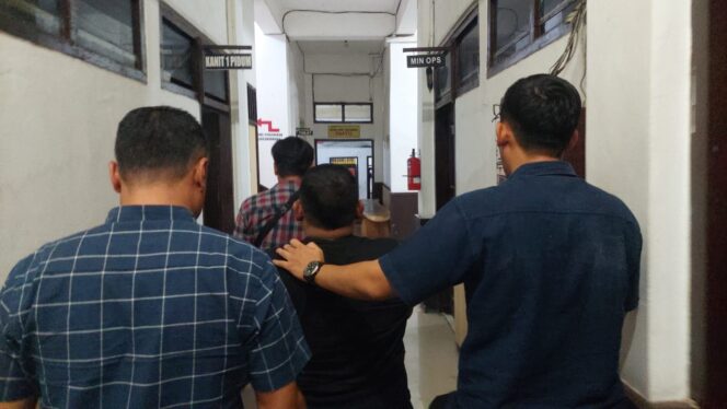 
					DITAHAN: Terduga pelaku penipuan, Sigit (memakai baju hitam dan diapit 2 petugas kepolisian) saat digelandang anggota Polres Probolinggo Kota. (foto: Hafiz Rozani).
