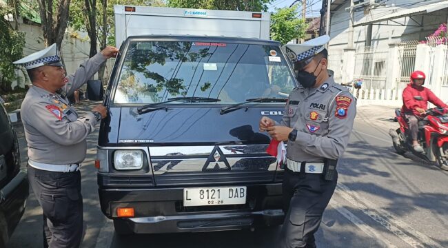 BAGI BENDERA: Anggota Satlantas Polres Probolinggo Kota saat membagikan bendera merah putih ke pengguna kendaraan. (foto: istimewa)
