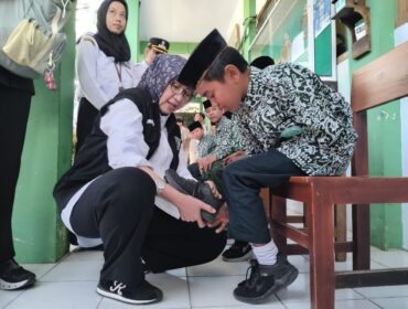 Bupati Indah Amperawati memasangkan sepatu pada kaki murid di SMP Wahidiyah, Senduro.  (Foto: Asmadi).
