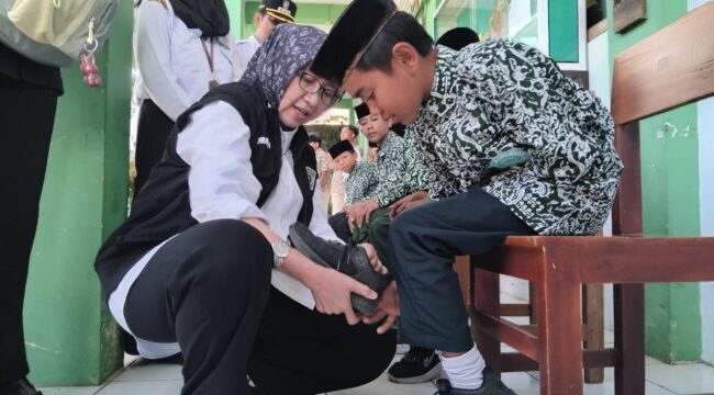 Bupati Indah Amperawati memasangkan sepatu pada kaki murid di SMP Wahidiyah, Senduro.  (Foto: Asmadi).
